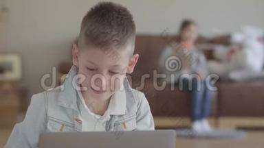 肖像可爱的小男孩坐在笔记本电脑上，小女孩，他的孪生妹妹在沙发上吹肥皂泡。